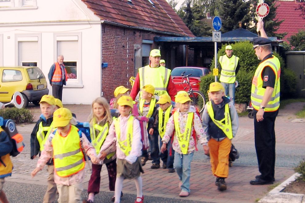 Schülerlotsen führen Kinder über die Straße, alle tragen Warnwesten