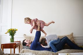 Ein Mann spielt mit zwei Kindern auf einem Sofa.