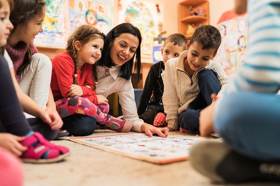 Eine Frau und eine Gruppe Kinder sehen sich gemeinsam eine Buchstabentafel an.