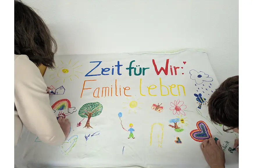 2 Menschen gestalten ein Plakat mit der Aufschrift "Zeit für Wir: Familie leben".
