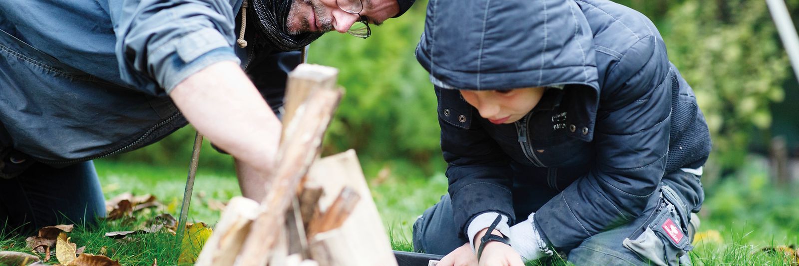 Ein Erwachsener Mann und ein Kind bauen ein Lagerfeuer im Wald