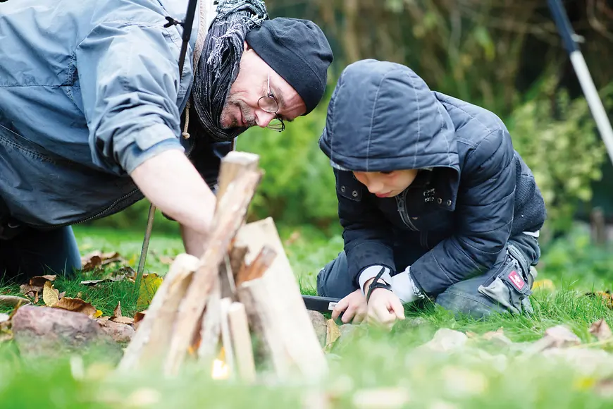 Ein Erwachsener Mann und ein Kind bauen ein Lagerfeuer im Wald