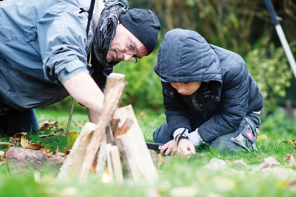 Ein Erwachsener Mann und ein Kind bauen ein Lagerfeuer im Wald
