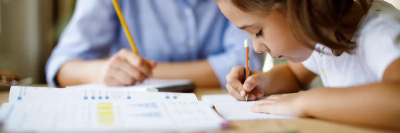 Kind und Erwachsene beim gemeinsamen Lernen am Tisch.